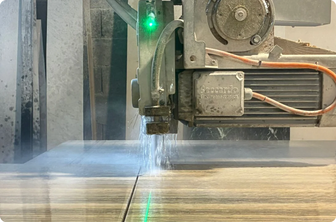 Scie à pont laser découpant précisément une dalle de marbre beige dans l'atelier de notre artisans marbrier.